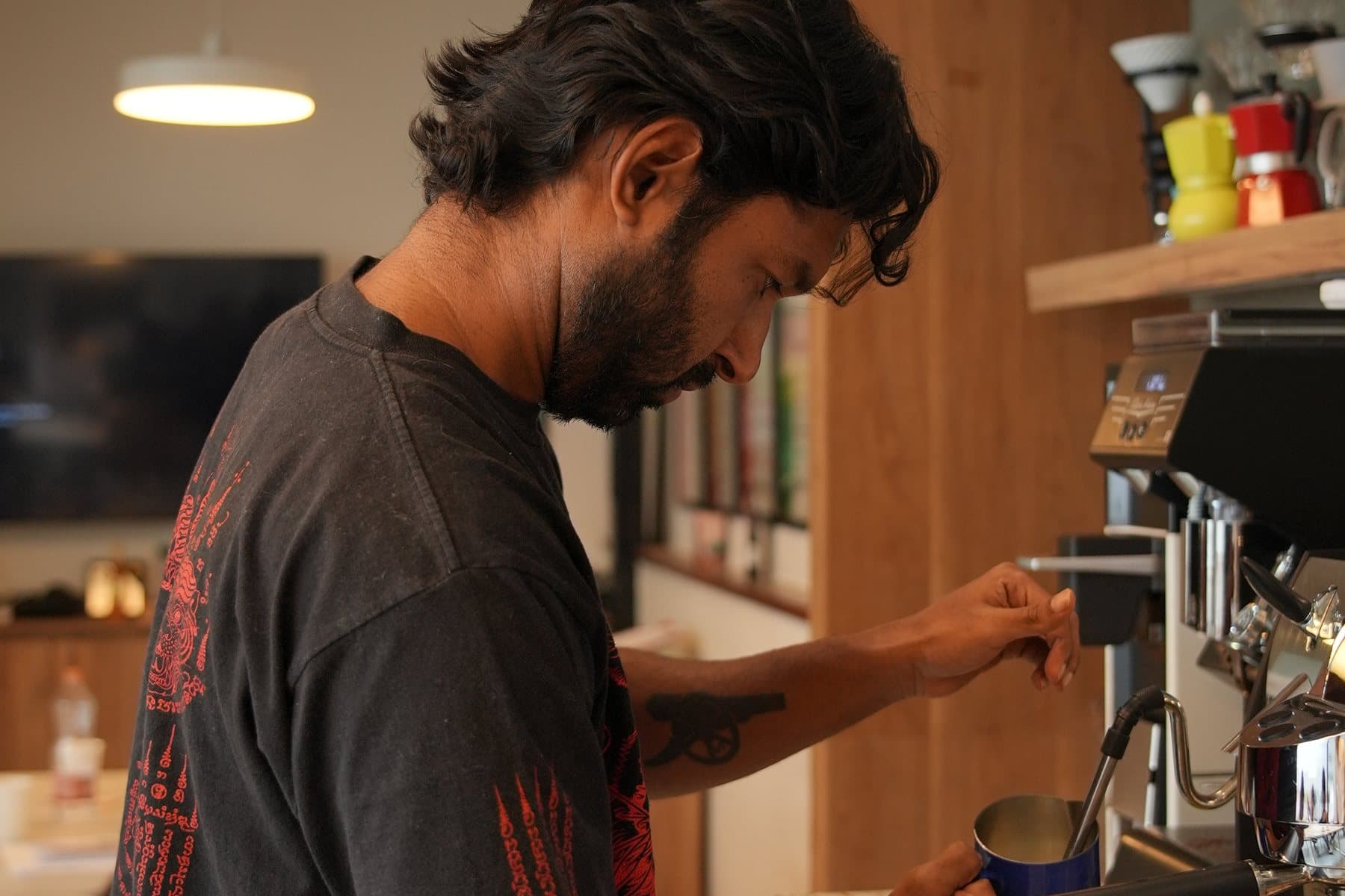 A barista at a professional espresso machine, steaming milk in a jug at the steam wand.